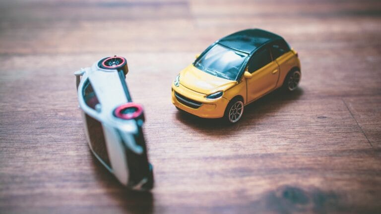 Two toy cars on a wooden desk, illustrating a collision, symbolizing factors that determine the severity of auto accident injuries