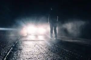 pedestrian in road at night with low visibility and car headlights approaching
